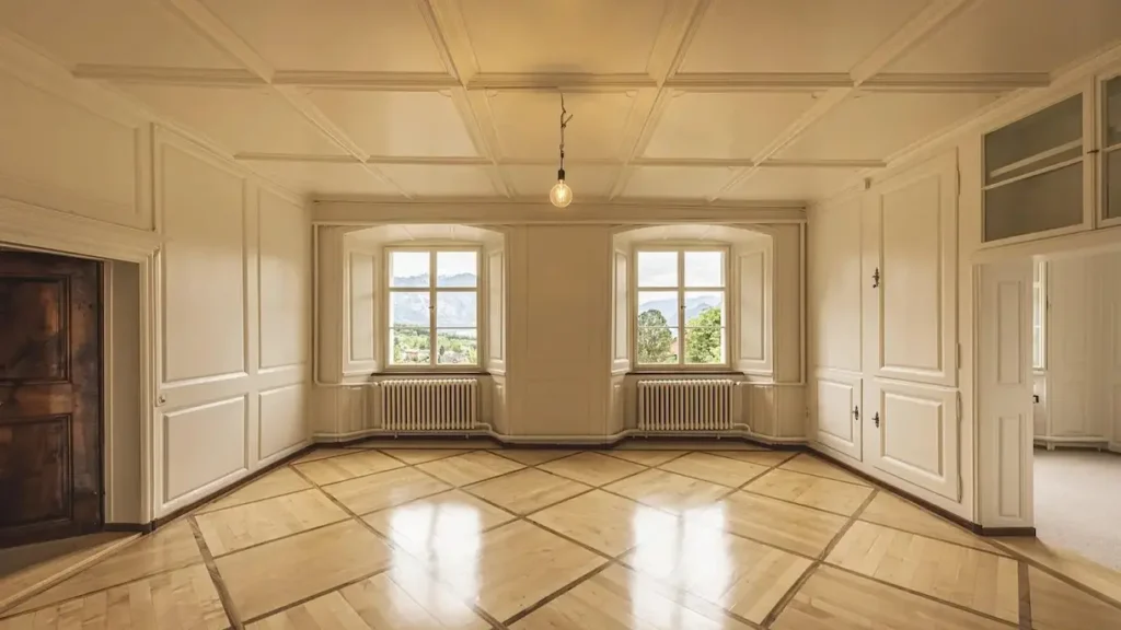 따뜻한 햇살이 드는 넓고 비어있는 방의 모습. 나무 바닥과 창문 너머로 보이는 풍경이 새로운 시작을 앞두고 인테리어를 구상하며 설레는 마음을 표현하고 있습니다.