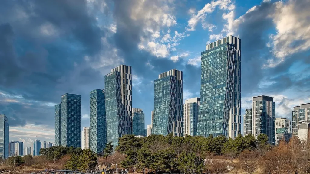 현대적인 고층 빌딩과 푸른 공원이 어우러진 인천 송도의 전경. 맑은 하늘 아래 펼쳐진 탁 트인 도시 풍경이 쾌적하고 건강한 웰니스 라이프스타일을 상징합니다.