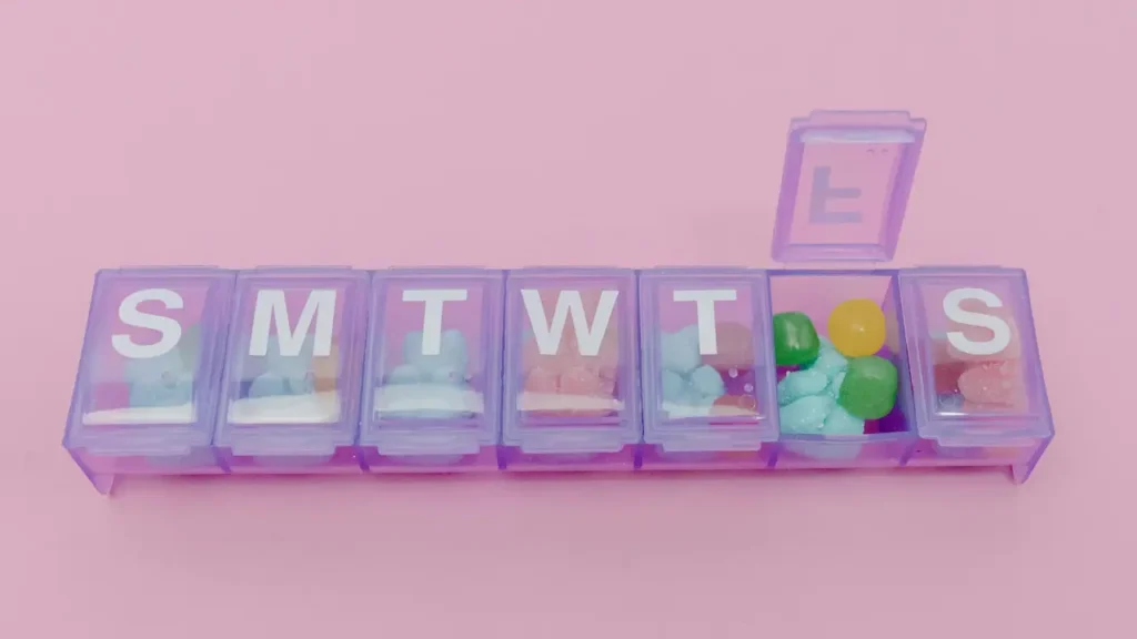 분홍색 배경 위에 놓인 보라색 주간 약통. 각 칸마다 영양제 대신 알록달록한 곰돌이 젤리가 담겨 있어 웰니스 습관을 재미있게 표현한 이미지.